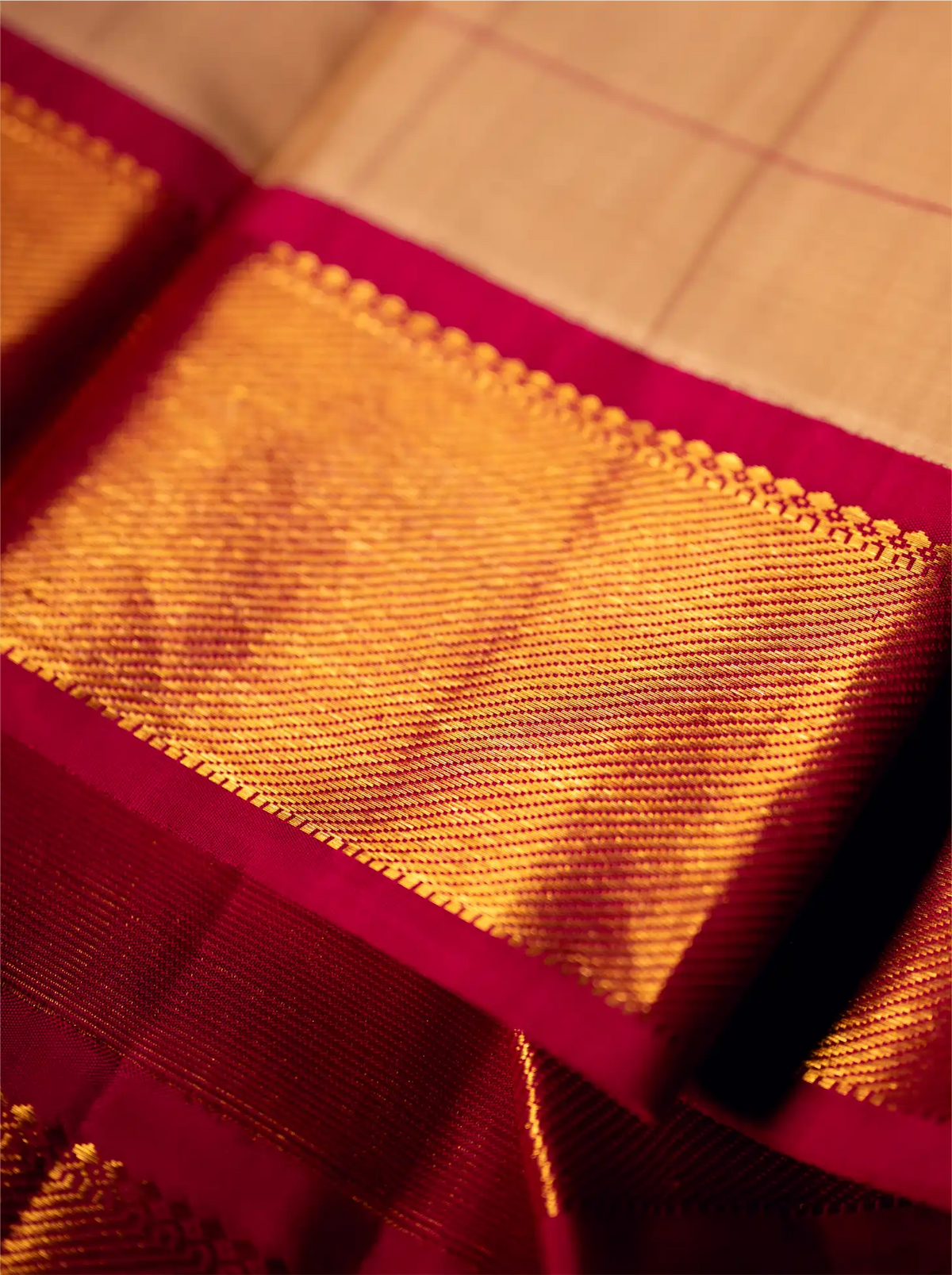 Close-up view of a folded handwoven Kanjivaram silk saree featuring a rich golden-yellow woven texture with fine grid lines and a contrasting deep magenta border adorned with intricate zari detailing.