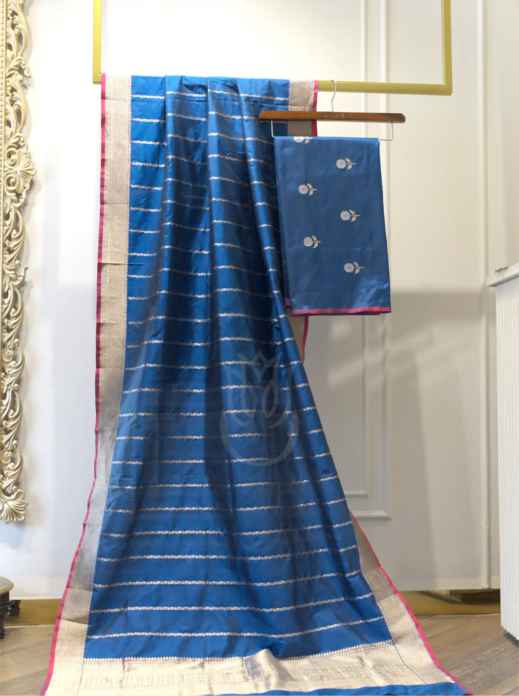 Folded royal blue handwoven Kora Katan silk suit fabric featuring silver floral bootis next to a matching gold zari striped dupatta with a contrast pink border.
