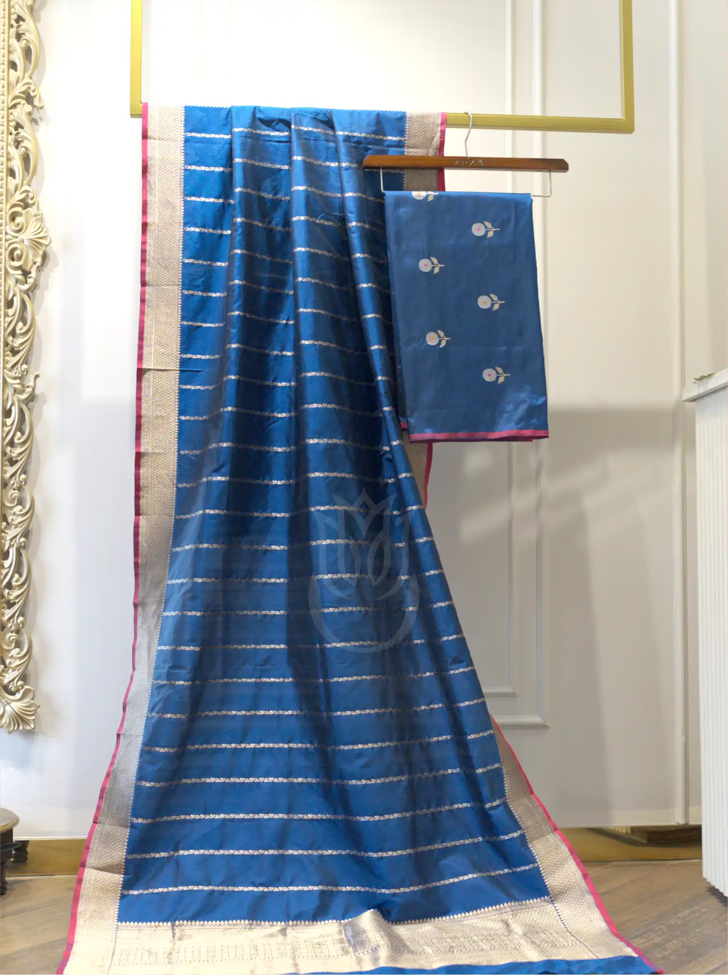 Folded royal blue handwoven Kora Katan silk suit fabric featuring silver floral bootis next to a matching gold zari striped dupatta with a contrast pink border.