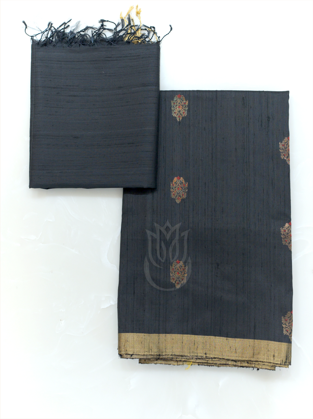 Folded charcoal black handwoven Matka silk suit fabric with gold and red woven bootis paired with a matching tissue border dupatta with fringe tassels on a plain background