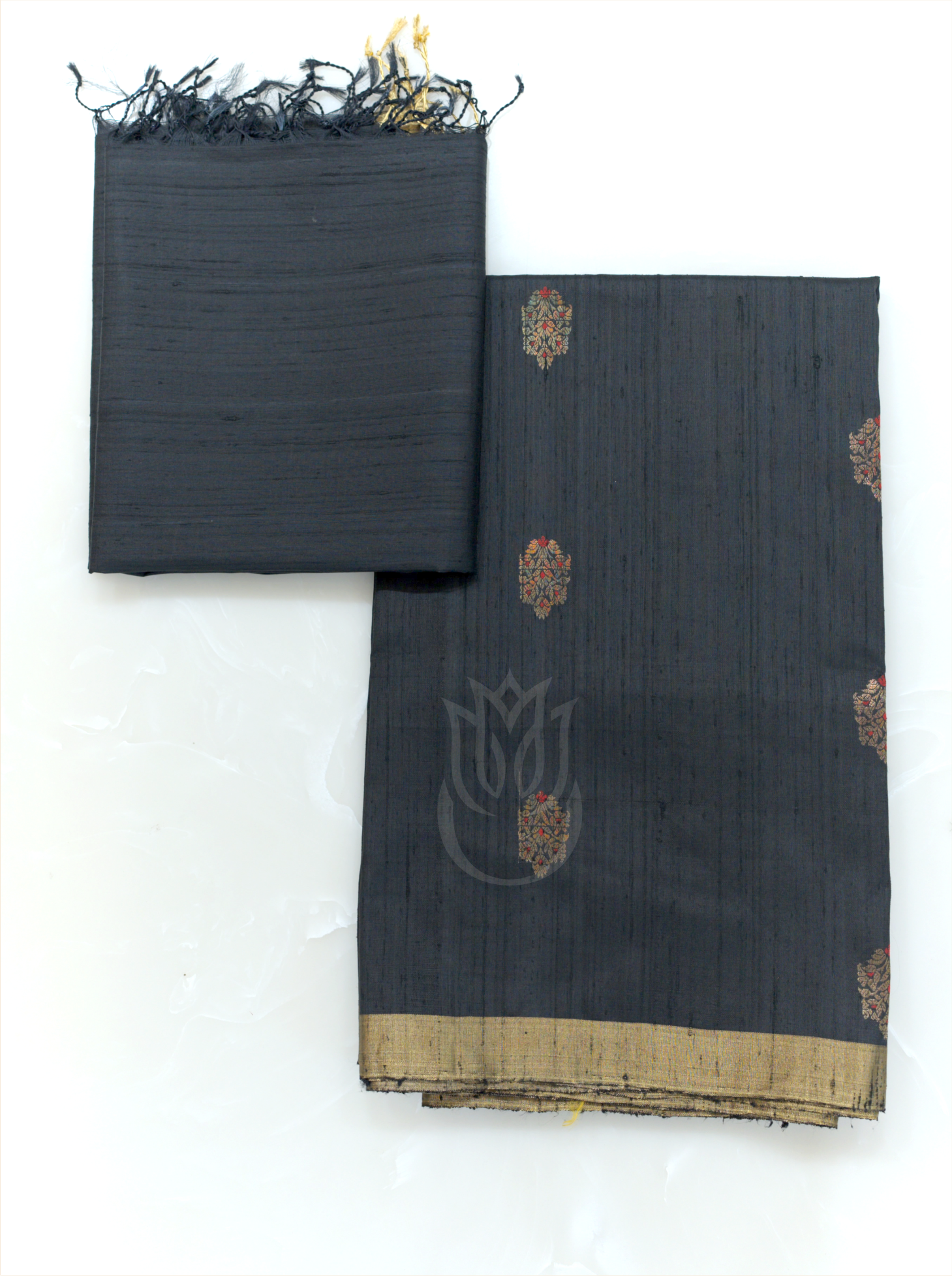 Folded charcoal black handwoven Matka silk suit fabric with gold and red woven bootis paired with a matching tissue border dupatta with fringe tassels on a plain background