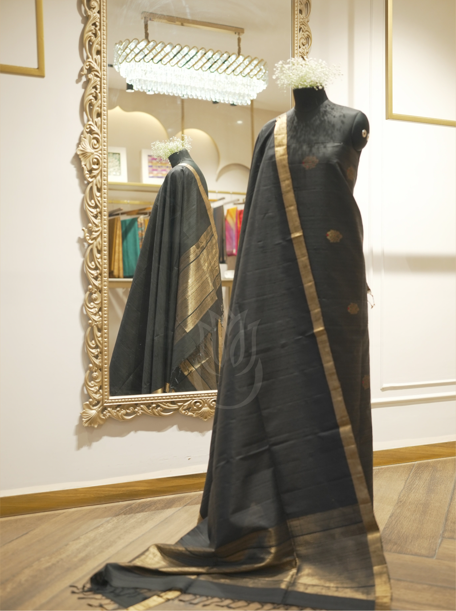 Full-length display of a charcoal black handwoven Matka silk suit on a mannequin, showcasing a draped dupatta with an antique gold zari border reflected in a decorative mirror