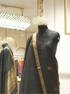 Handwoven Matka silk charcoal black suit fabric with gold and red bootis, displayed on a mannequin torso with a gold tissue border dupatta in a boutique setting