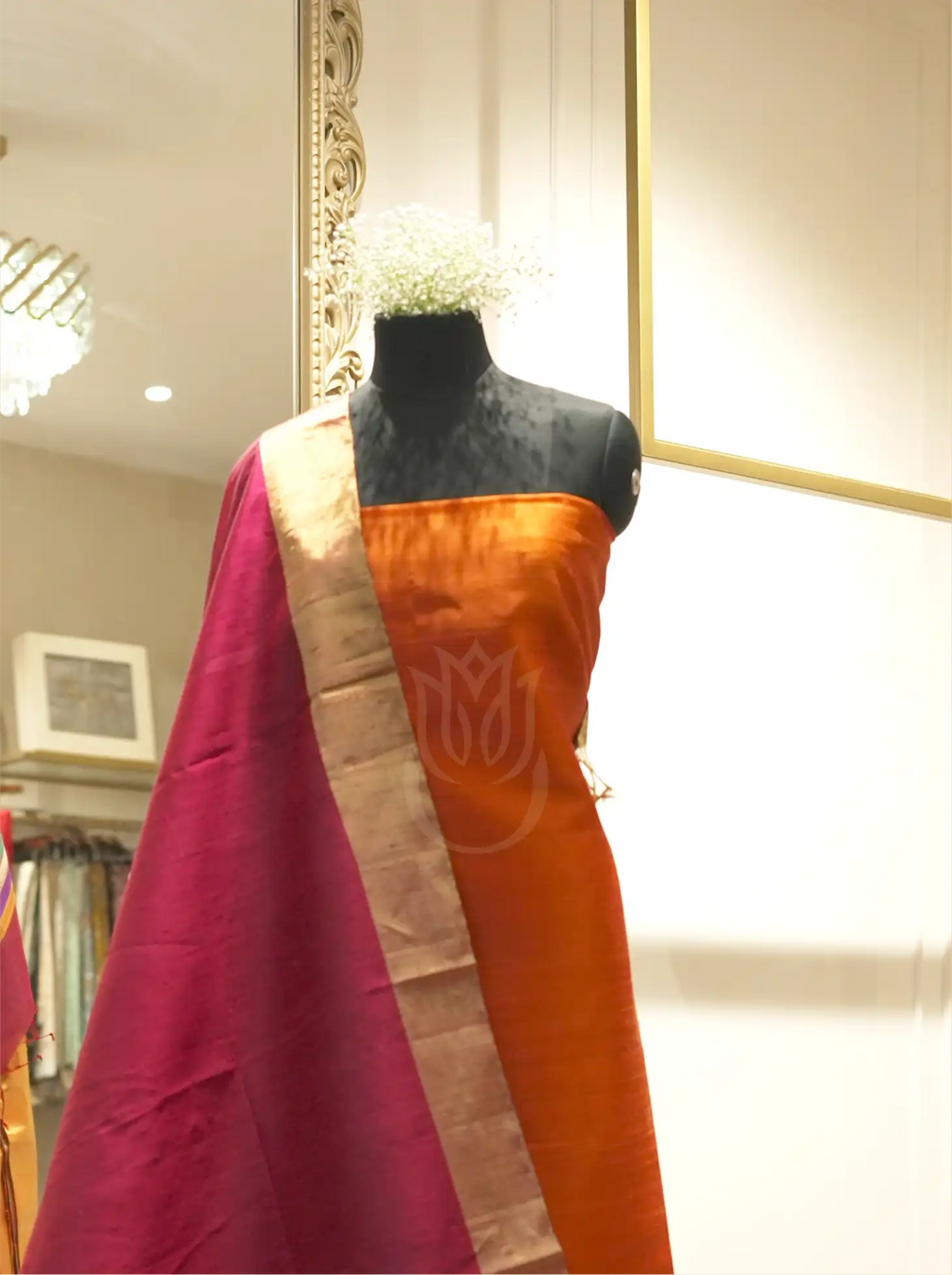 Handwoven orange silk suit fabric draped with a deep magenta Matka silk dupatta featuring a gold tissue border, displayed on a black mannequin torso in a boutique setting