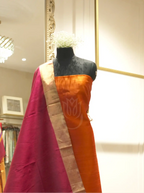 Handwoven orange silk suit fabric draped with a deep magenta Matka silk dupatta featuring a gold tissue border, displayed on a black mannequin torso in a boutique setting