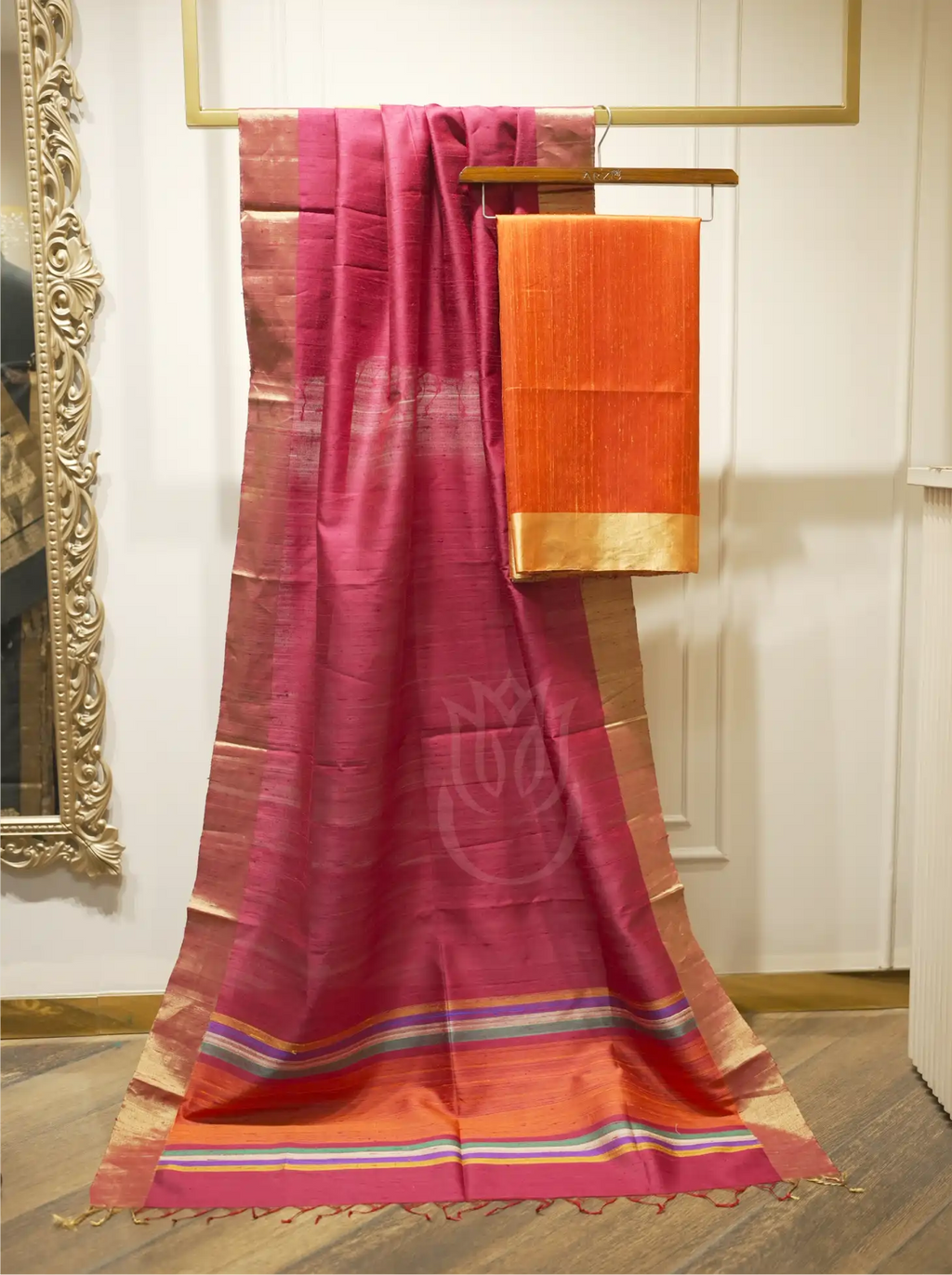 Handwoven Matka silk orange suit fabric draped alongside a deep magenta dupatta with gold tissue borders and multi-color striped palla on a wooden hanger stand
