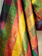 Close-up of a draped handwoven multicolor brocade silk saree displaying intricate square-framed geometric and floral motifs in vibrant yellow, emerald green, magenta pink, and purple vertical panels.