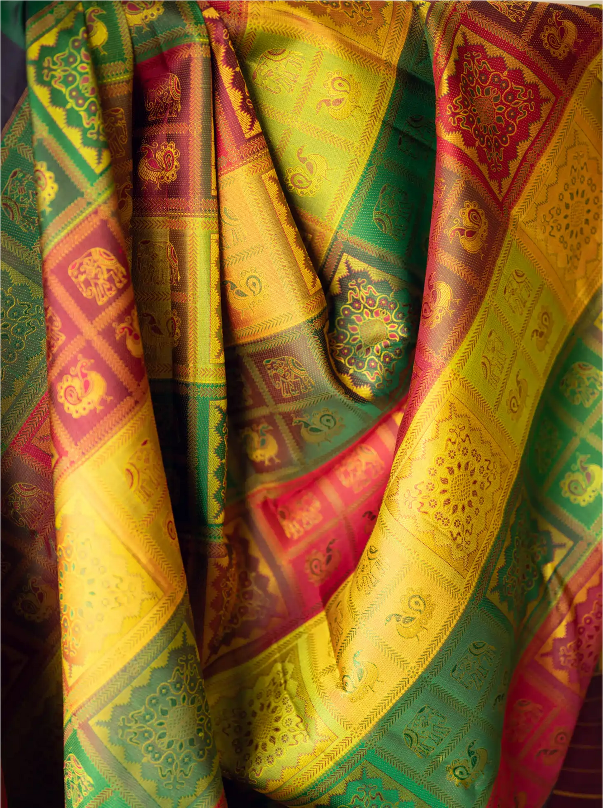 Detailed shot of draped handwoven brocade silk fabric featuring vibrant yellow, green, red, and gold vertical panels filled with intricate traditional woven animal and floral motifs.