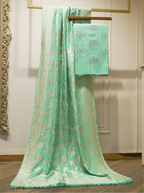 Seafoam green handwoven Munga silk suit fabric draped alongside an intricately woven Phulkari floral jaal dupatta with gold zari borders on a wooden stand in a boutique