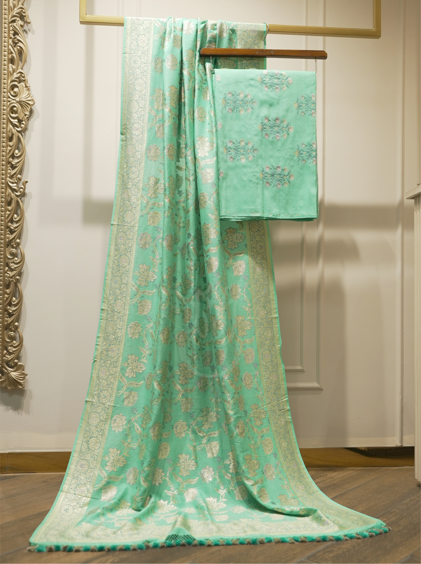 Seafoam green handwoven Munga silk suit fabric draped alongside an intricately woven Phulkari floral jaal dupatta with gold zari borders on a wooden stand in a boutique