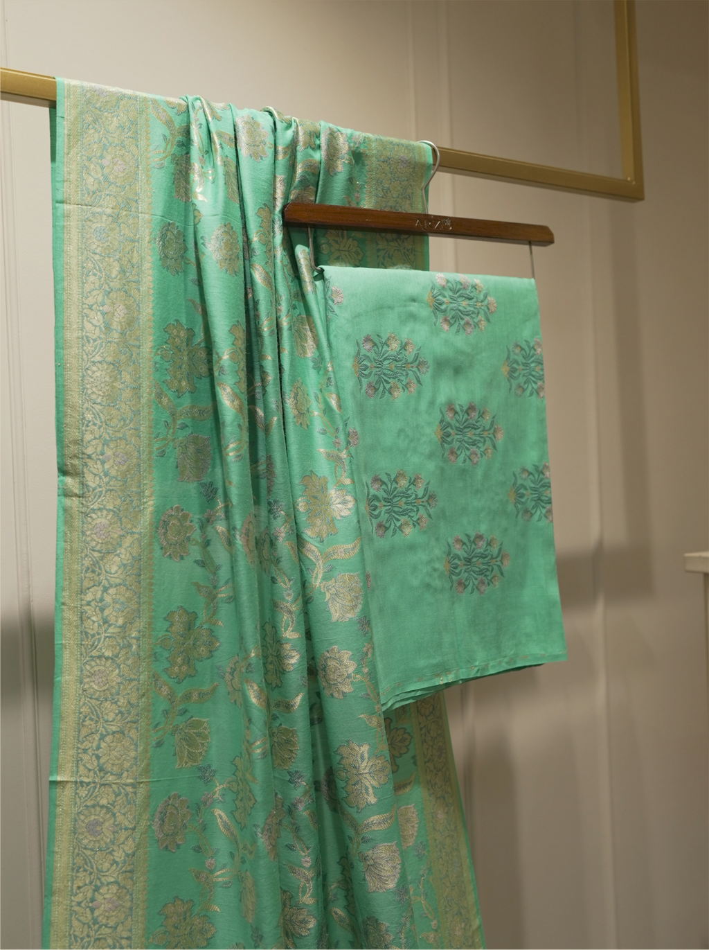 Seafoam green handwoven Munga silk dupatta with woven gold zari borders draped alongside matching floral bootis suit fabric on a wooden hanger display