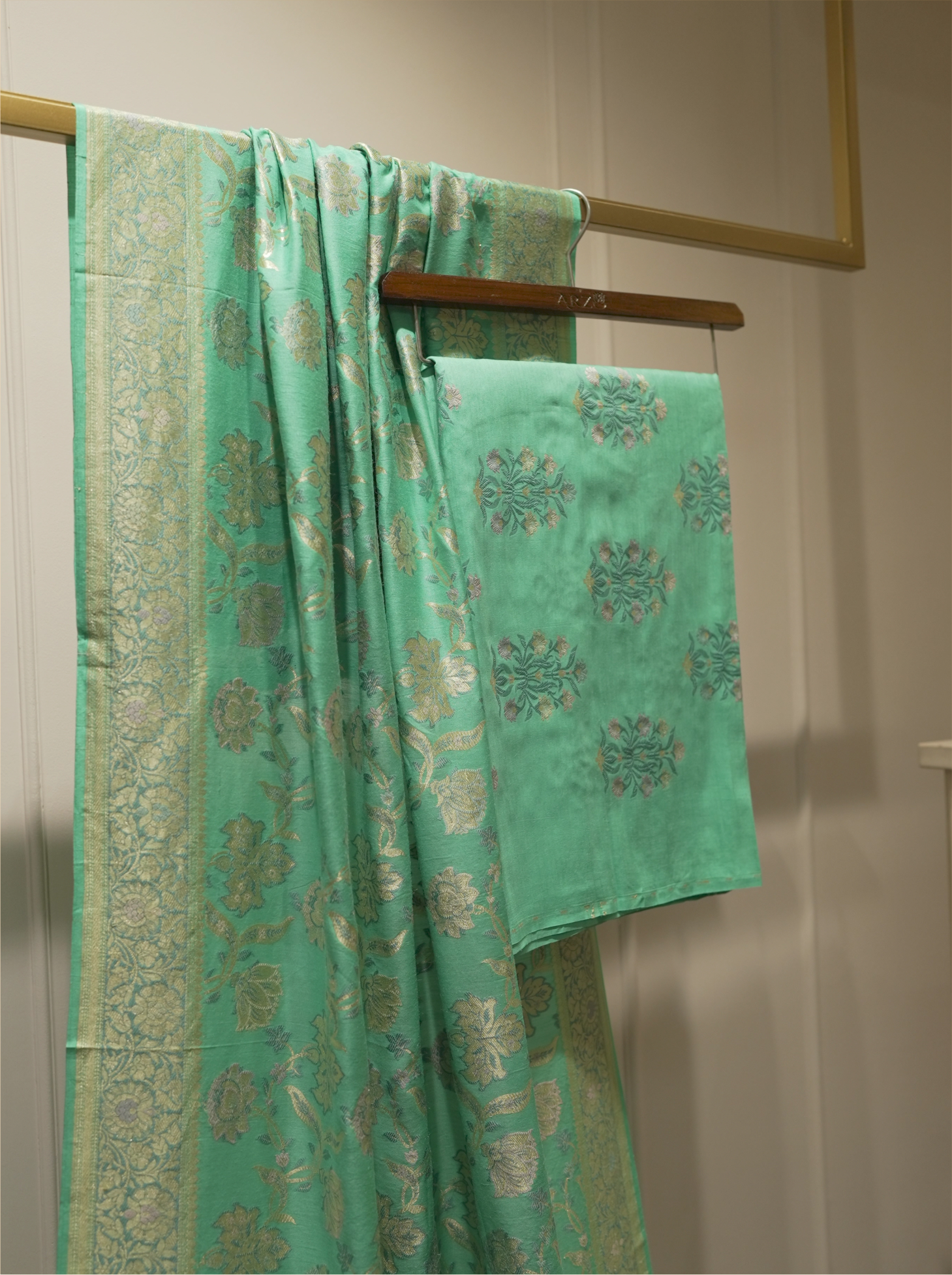 Seafoam green handwoven Munga silk dupatta with woven gold zari borders draped alongside matching floral bootis suit fabric on a wooden hanger display