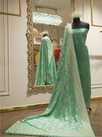 Full-length display of a seafoam green handwoven Munga silk suit draped on a mannequin, styled with an intricately woven Phulkari floral jaal dupatta reflected in a gold ornate mirror