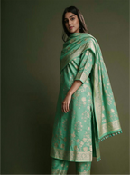 Woman modeling a handwoven seafoam green Munga silk suit featuring silver zari floral bootis, styled with a draped matching Phulkari woven dupatta against a olive green background