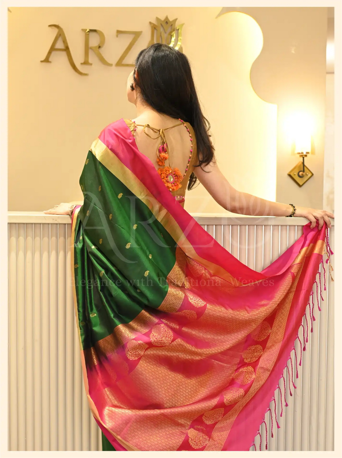 Back view of a model showcasing the vibrant pink and gold zari pallu drape of a handwoven dark green Mysore silk saree.