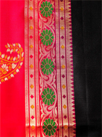 Close-up shot showing the side border of a handwoven pure Paithani silk saree, displaying a vibrant green and orange floral zari pattern alongside a rich red selvedge and black silk body weave.