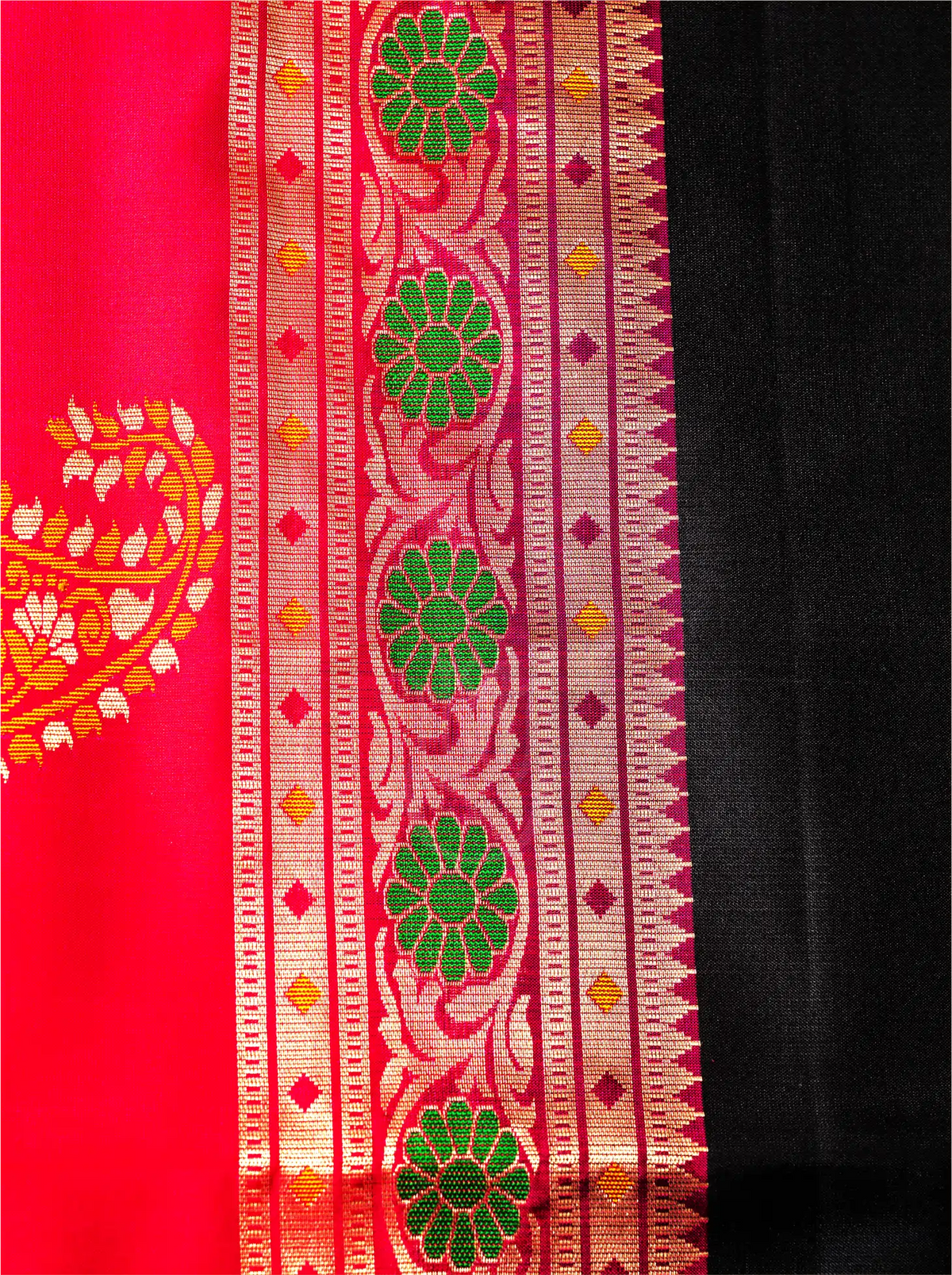 Close-up shot showing the side border of a handwoven pure Paithani silk saree, displaying a vibrant green and orange floral zari pattern alongside a rich red selvedge and black silk body weave.