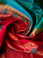 Close-up top view of a swirling handwoven Paithani silk saree showcasing a lustrous peacock teal green fabric draped alongside a vibrant red pallu intricately decorated with golden zari weaving, featuring geometric borders, floral patterns, and peacock motifs.