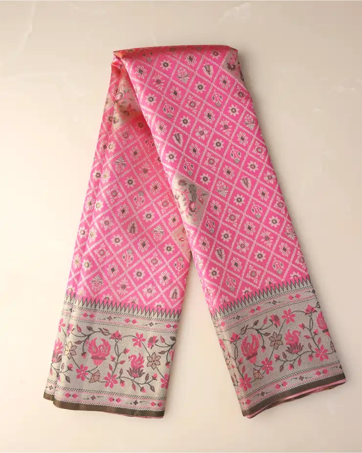 Folded length of a pink tissue Patola Kanjivaram silk saree showcasing geometric grid patterns and a woven floral zari border against a neutral background.
