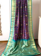 Draped handwoven purple and green Patola Kanjivaram silk saree with intricate red-purple geometric motifs and a wide teal gold zari border.