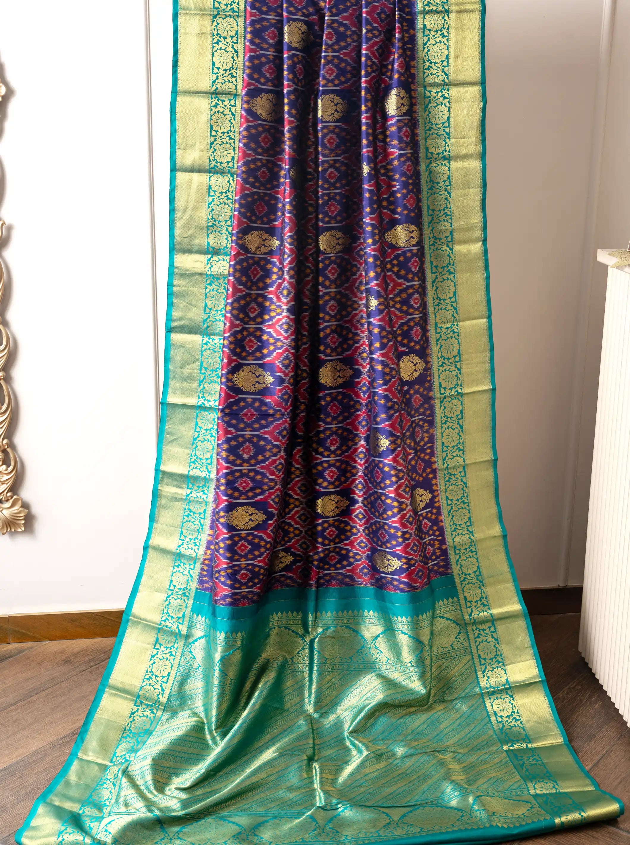 Draped handwoven purple and green Patola Kanjivaram silk saree with intricate red-purple geometric motifs and a wide teal gold zari border.