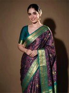 Woman modeling a handwoven purple and green Patola Kanjivaram silk saree with gold zari border and teal blouse.