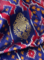 Macro shot of handwoven purple Patola silk saree showing a prominent metallic gold zari floral brocade motif over colorful ikat patterns.