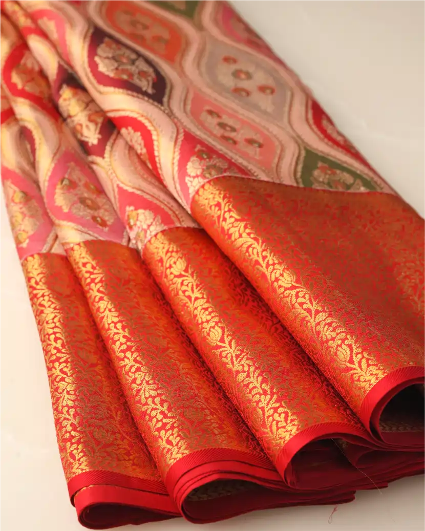 Neatly folded pleats of a handwoven champagne gold and orange Rangkart Kanchipuram silk saree showing the rich red gold zari woven border.