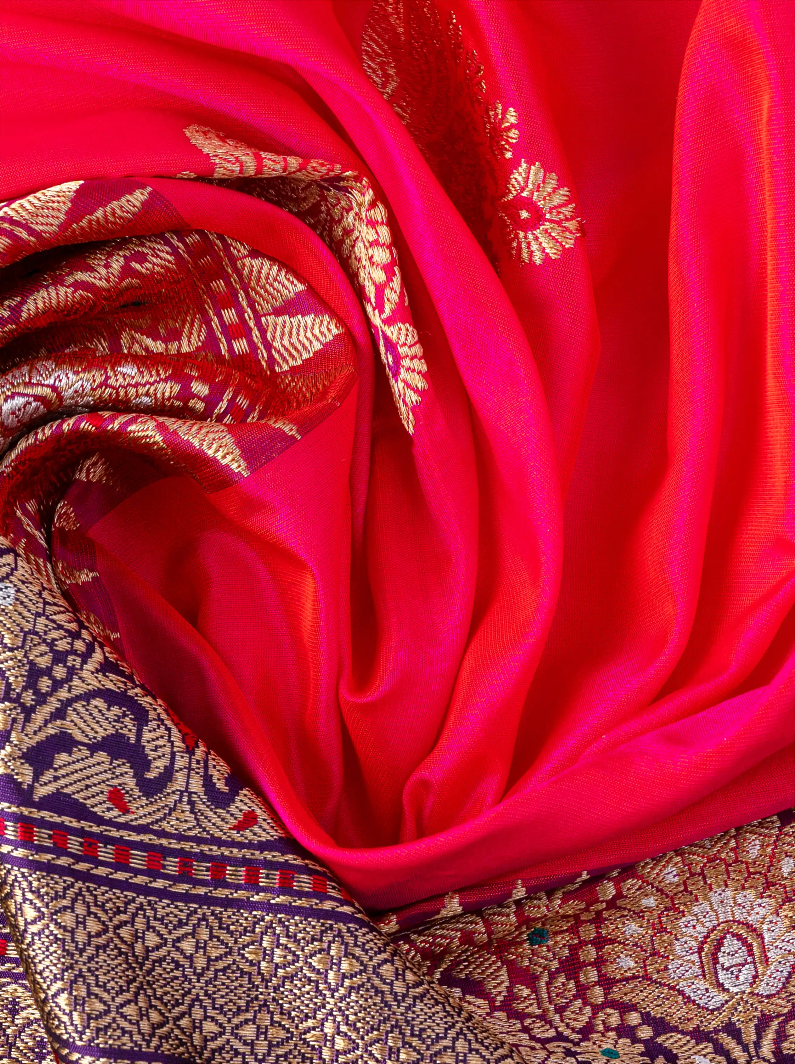 Close-up of draped red pure Katan silk saree showcasing metallic gold zari floral motifs and detailed purple and gold zari border.