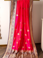 Handwoven red Katan silk saree with gold zari floral motifs and a detailed gold zari border draped on a wooden hanger.