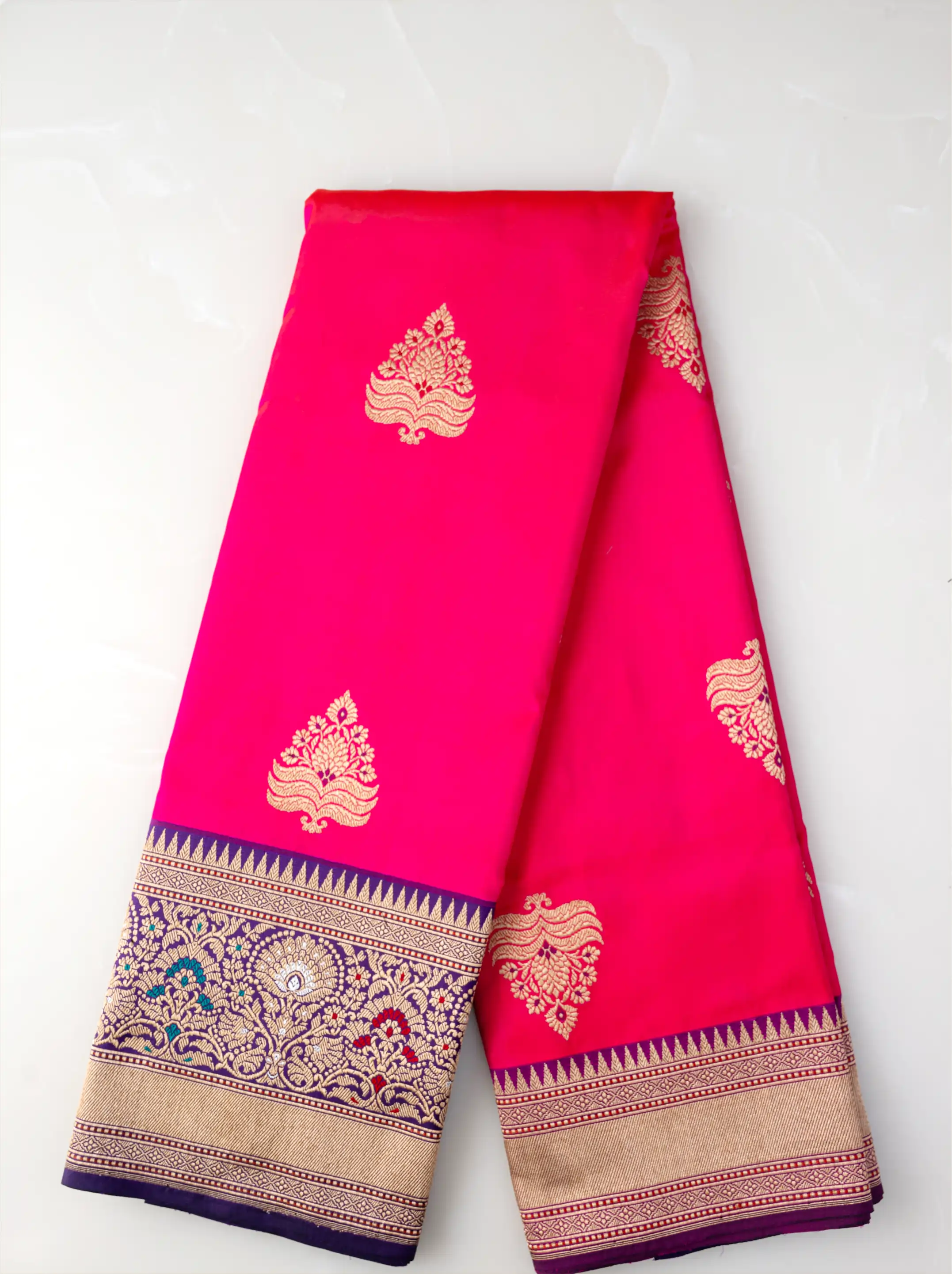 Folded handwoven red pure Katan silk saree showcasing gold zari floral motifs and a rich ornate gold zari border.