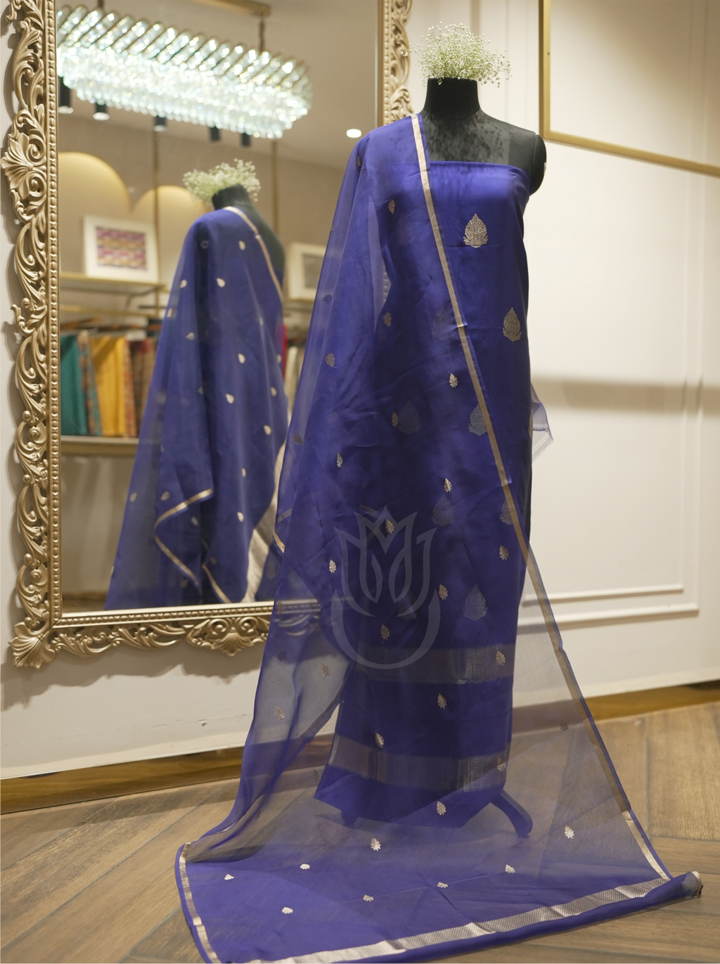 Full-length display of a royal blue handwoven silk suit draped on a mannequin, styled with a matching sheer dupatta featuring gold zari floral motifs and woven borders, set near an ornate gold mirror