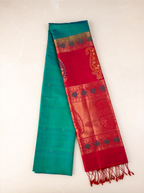 Neatly folded handwoven peacock teal green Paithani silk saree showcasing a rich, contrasting crimson red pallu and border adorned with intricate gold zari woven floral and peacock motifs, finished with delicate red tassels at the edge against a light background.