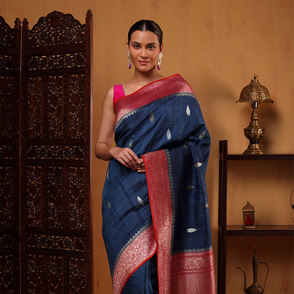 A woman posing in a Midnight Azure pure Tussar georgette silk saree featuring a tri-color weave border with pink accents, paired with a matching pink sleeveless blouse.