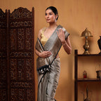 Side profile view of a woman eleganty draping the Ivory Noir Tanchoi Banarasi Silk Saree next to a dark wooden screen partition.
