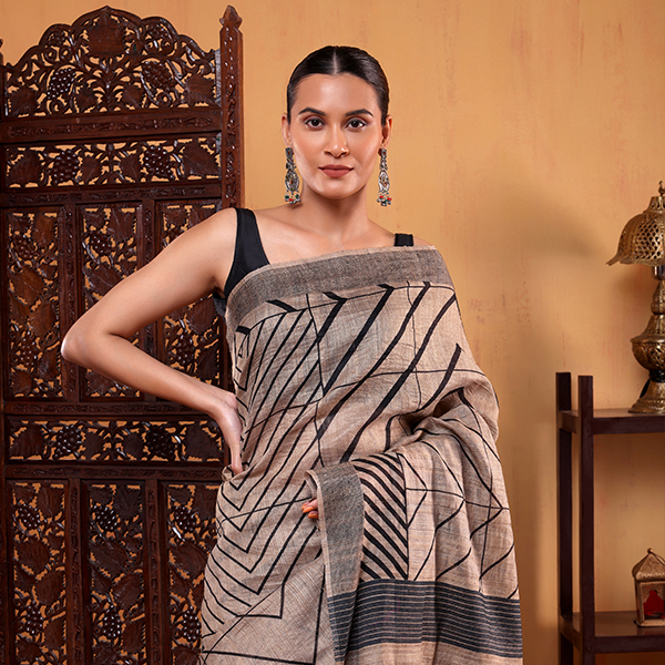 A woman posing in an ivory Tussar silk saree featuring a black satin border and modern black geometric stripe patterns, styled with a black sleeveless blouse.