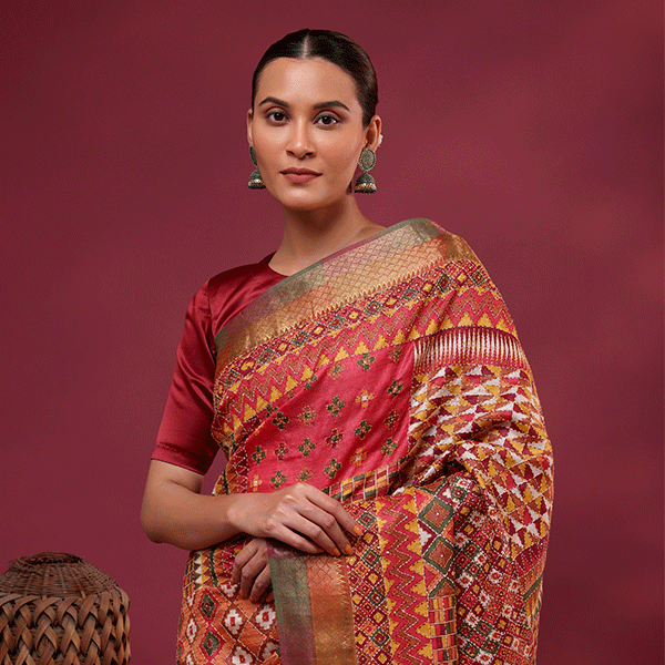 A woman modeling a Kaleidoscope Kantha Tussar Silk Saree with multicolored geometric patterns and a matching blouse against a maroon background.