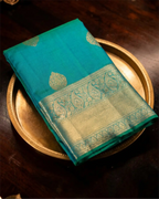 A neatly folded dark teal Kanjivaram silk saree, highlighting the richness of the zari work.