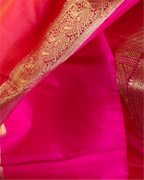 Close-up of a vibrant pink Kanjivaram silk saree featuring a wide, ornate gold zari woven border with traditional paisley and floral patterns.