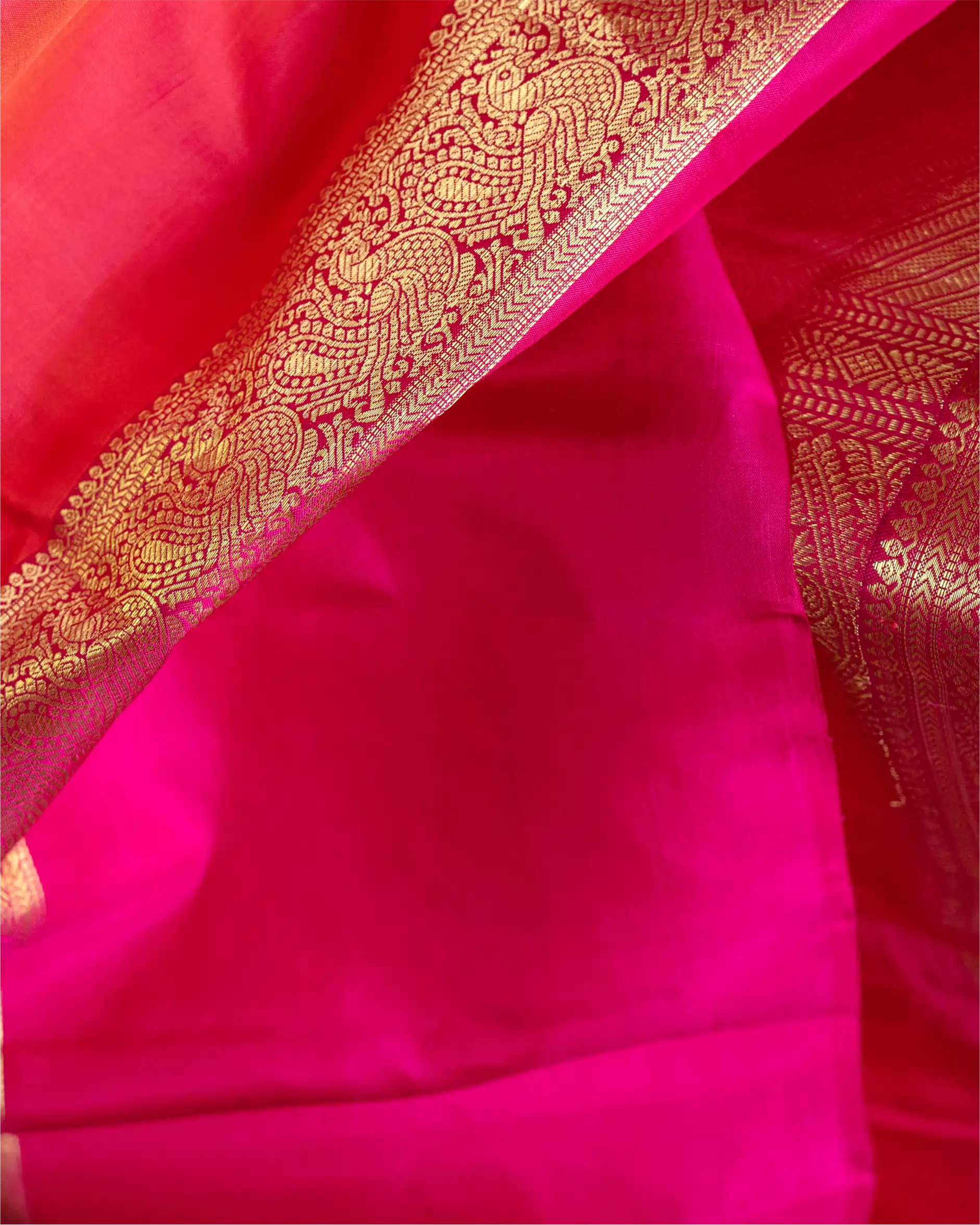 Close-up of a vibrant pink Kanjivaram silk saree featuring a wide, ornate gold zari woven border with traditional paisley and floral patterns.
