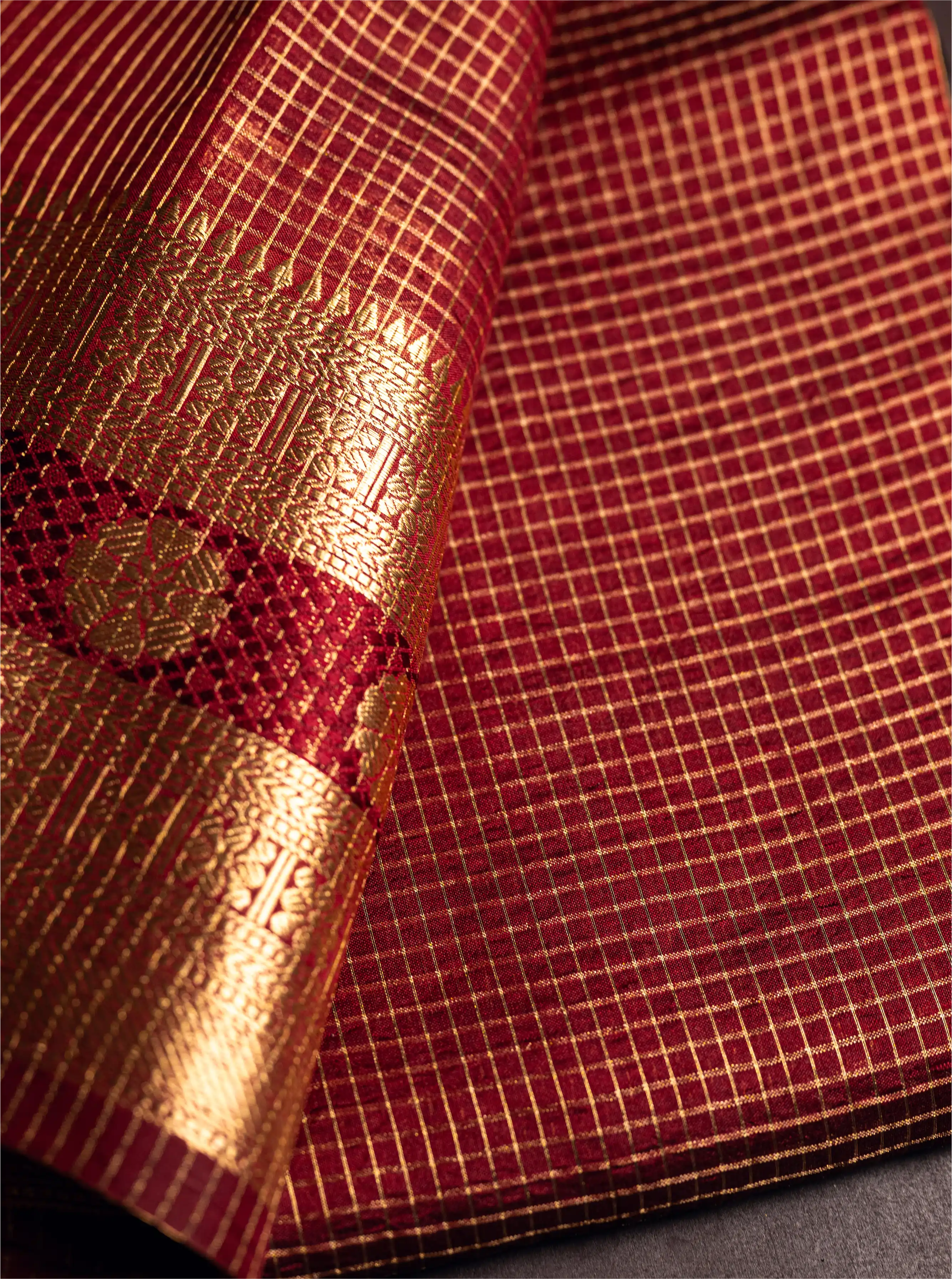 Close-up of a maroon Handwoven Pure Katan Silk Saree showcasing the intricate gold zari floral border and the traditional grid check pattern.