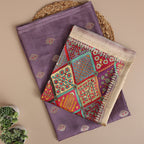A flat-lay view of an elegant light purple handwoven silk suit set, paired with a vibrant, multicolored traditional dupatta featuring intricate patterns and a delicate gold zari border.