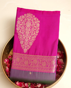 A folded magenta pink silk saree with a large gold floral zari motif and a decorative gold border, displayed on a gold-colored plate filled with pink rose petals