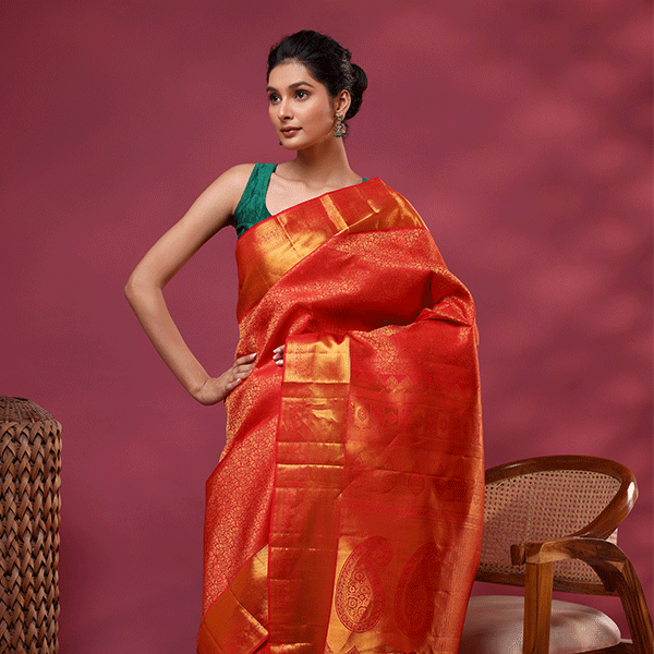 A woman posing in a vibrant pink magenta and gold Kanjivaram silk saree featuring an opulent gold zari pallu, styled with a contrasting dark green sleeveless blouse.