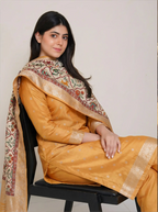 Woman wearing a traditional mango yellow Banarasi silk suit with an off-white Kalamkari dupatta, sitting on a chair.