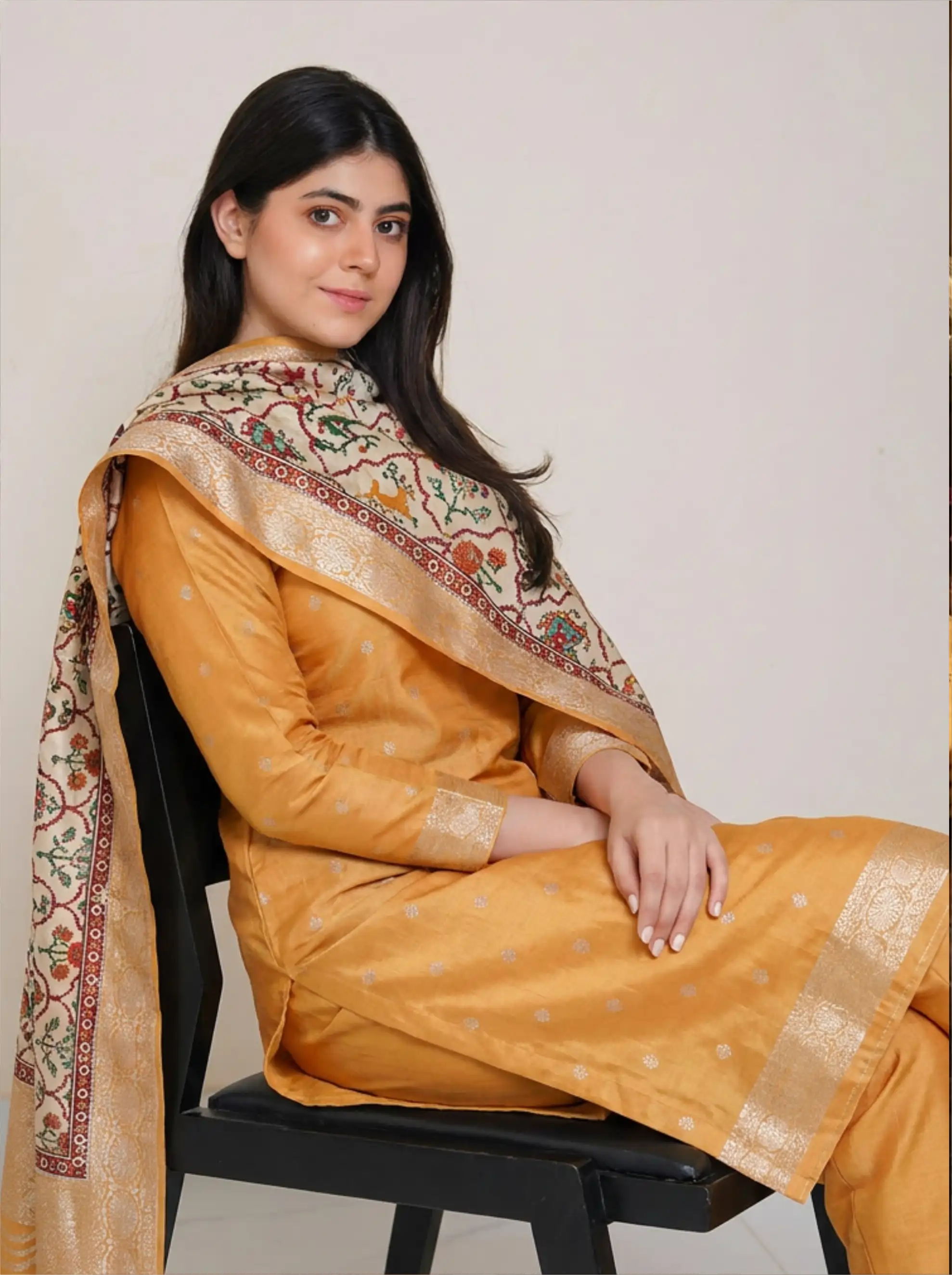 Woman wearing a traditional mango yellow Banarasi silk suit with an off-white Kalamkari dupatta, sitting on a chair.