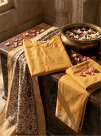 Mango yellow unstitched Banarasi silk suit fabric with a matching Kalamkari dupatta, styled on a wooden surface with rose petals.