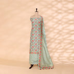 A mannequin displaying a traditional Banarasi Katan silk suit in mint green, featuring intricate floral Resham and gold Zari work against a soft textured background.