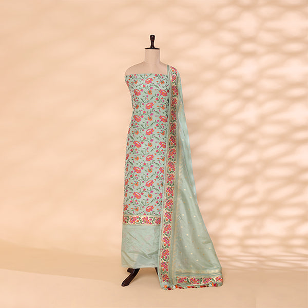 A mannequin displaying a traditional Banarasi Katan silk suit in mint green, featuring intricate floral Resham and gold Zari work against a soft textured background.