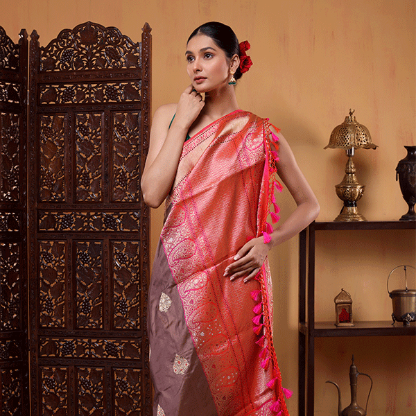 A woman modeling a mouse grey pure Katan silk saree featuring fine sona rupa bootas and a contrasting pink-purple zari border.